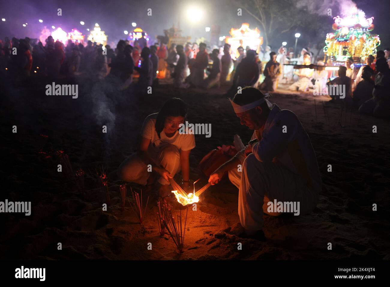 Los devotos Nicolas Tellier, de Francia, y Xin Li queman palos de joss en un ritual para enviar a los dioses al mar durante el último día del festival de los Nueve Dioses Emperadores Taoístas en Singapur el 4 de octubre de 2022. REUTERS/Edgar Su Foto de stock
