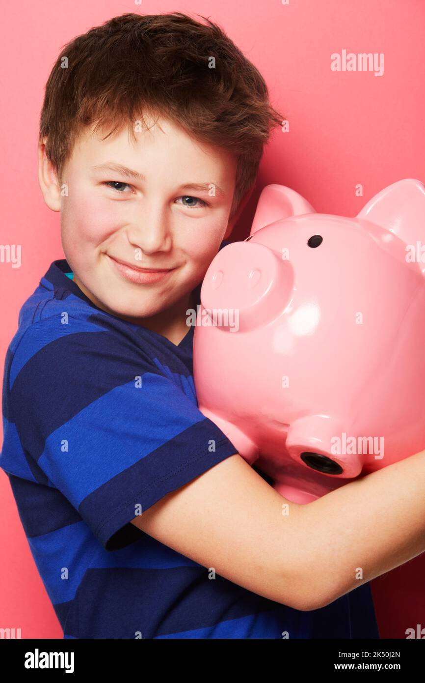 Abrazando su riqueza. Retrato de un niño sosteniendo su banco de cerdos. Foto de stock