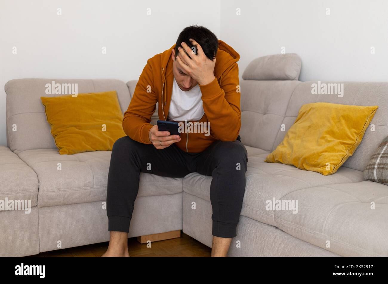 triste joven viendo al teléfono móvil en el sofá Foto de stock