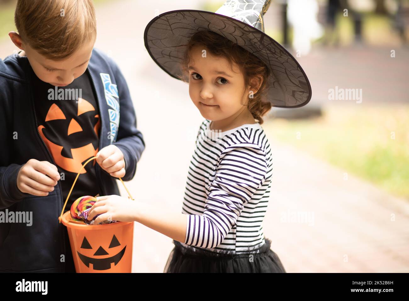 Pequeña chica cute con disfraz de bruja y chico sosteniendo un cubo de  calabaza Jack-o-linterna con dulces y dulces y dulces y sabores dulces. Los  niños engañan o tratan en Ha Fotografía