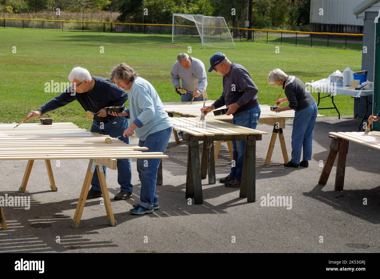St. Johnsville, Montgomery County, Nueva York: Los voluntarios pintan tablillas de madera durante la reparación de la tribuna en el campo de pelota de la comunidad. Foto de stock