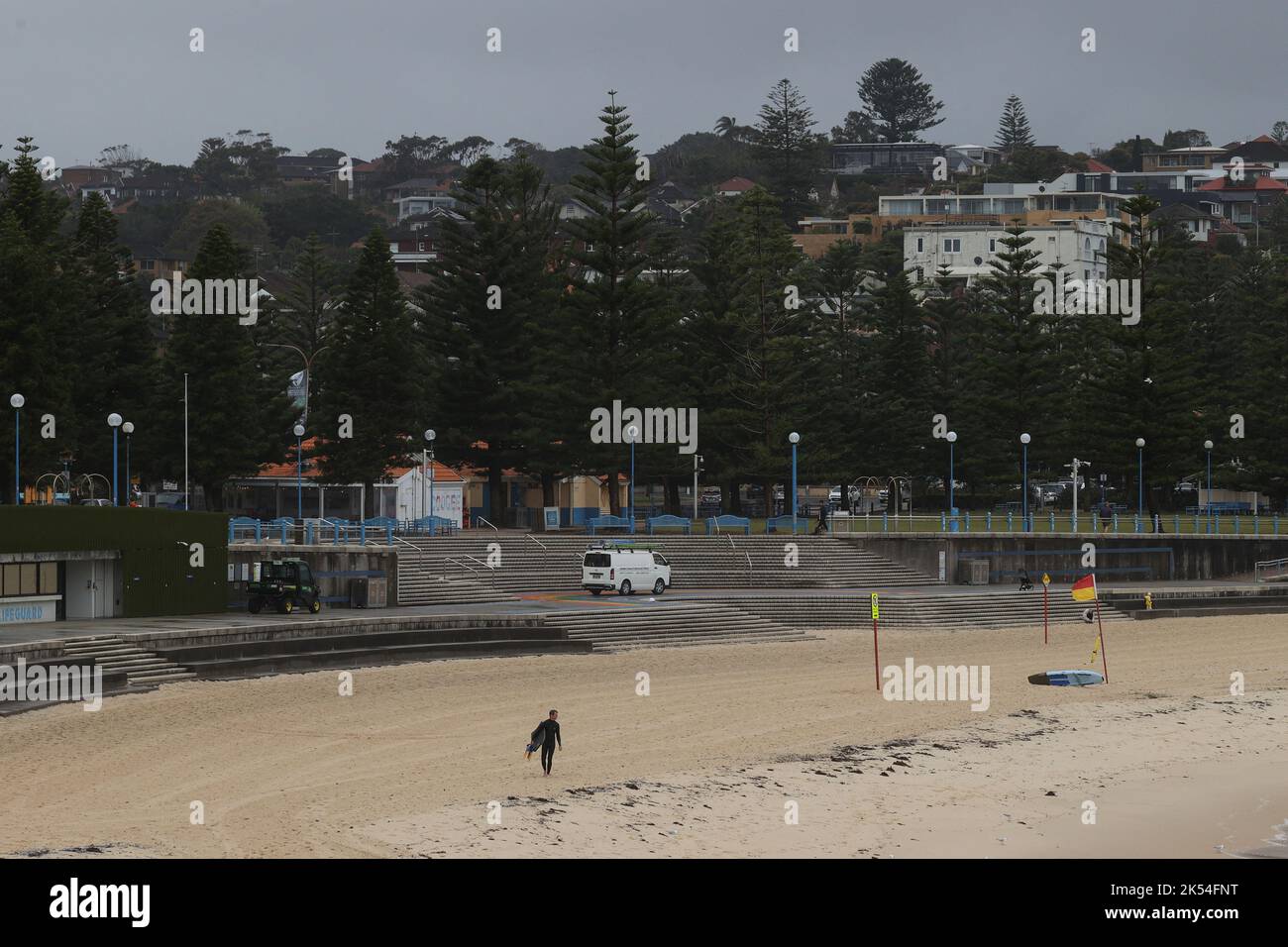 Una persona con traje de neopreno camina por una playa vacía de Coogee Beach durante el tiempo tormentoso, ya que las fuertes lluvias afectan a Sydney, Australia, 6 de octubre de 2022. REUTERS/Loren Elliott Foto de stock