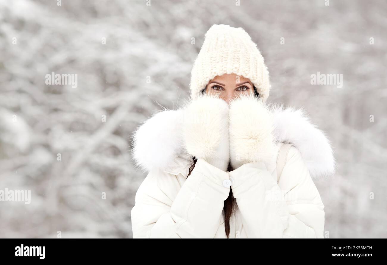 Mujer congelada en invierno frío al aire libre. Chica con ropa cálida,  chaqueta blanca de plumón con piel, sombrero y manoplas, cubriendo las  manos de su boca Fotografía de stock - Alamy