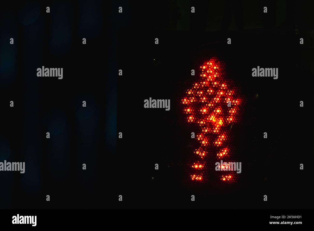El semáforo de peatones muestra una señal de stop roja con un cartel LED de hombre sobre fondo negro nocturno Foto de stock
