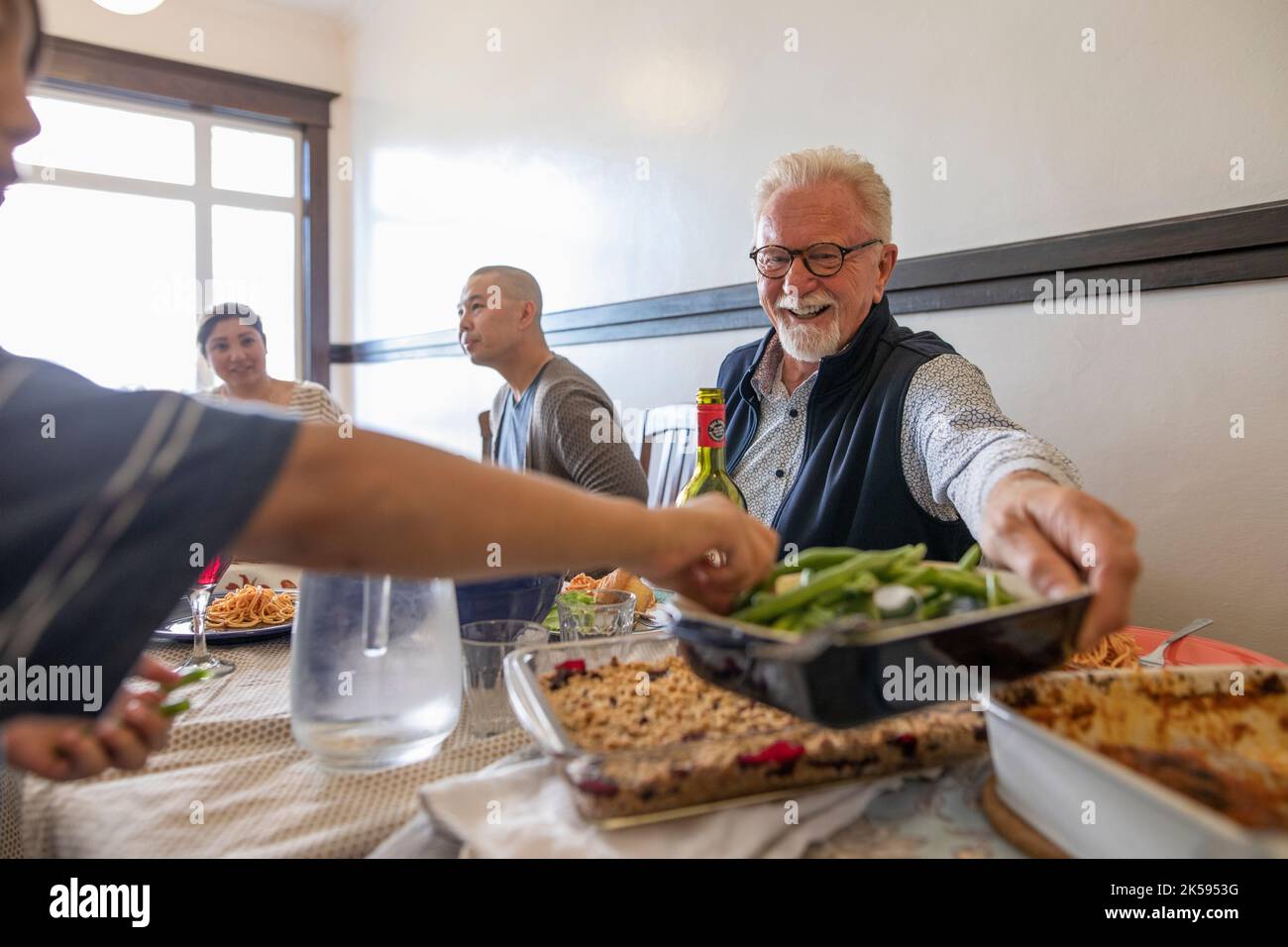 Sonriente anciano pasando comida al vecino, disfrutando la cena de la comunidad Foto de stock