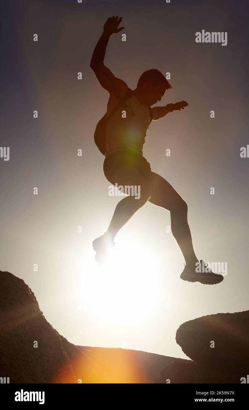 Sea audaz y tome riesgos. Una silueta de un hombre saltando sobre rocas. Foto de stock