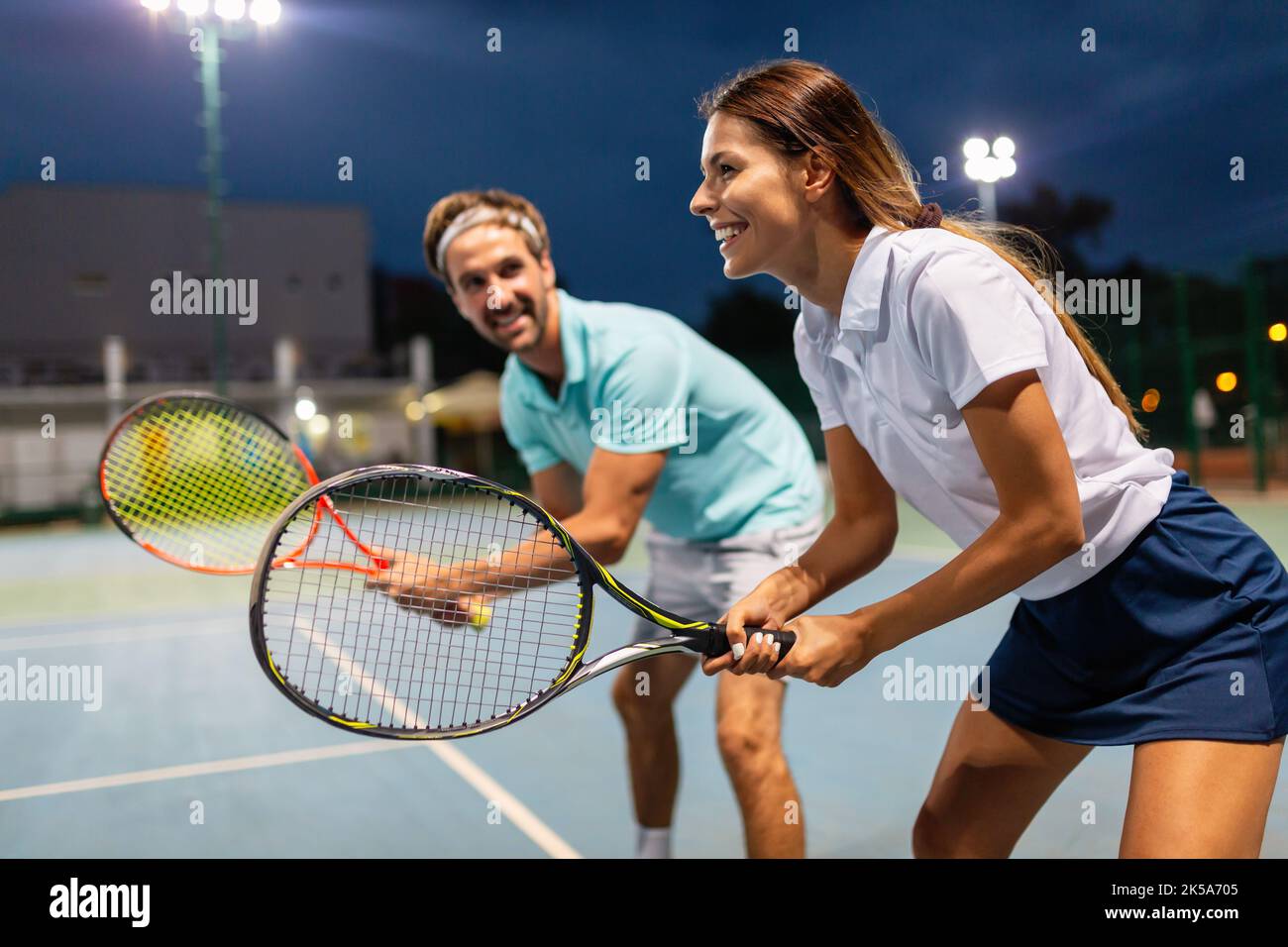 Pareja joven en pista de tenis. Hombre guapo y mujer atractiva están jugando al tenis. Foto de stock