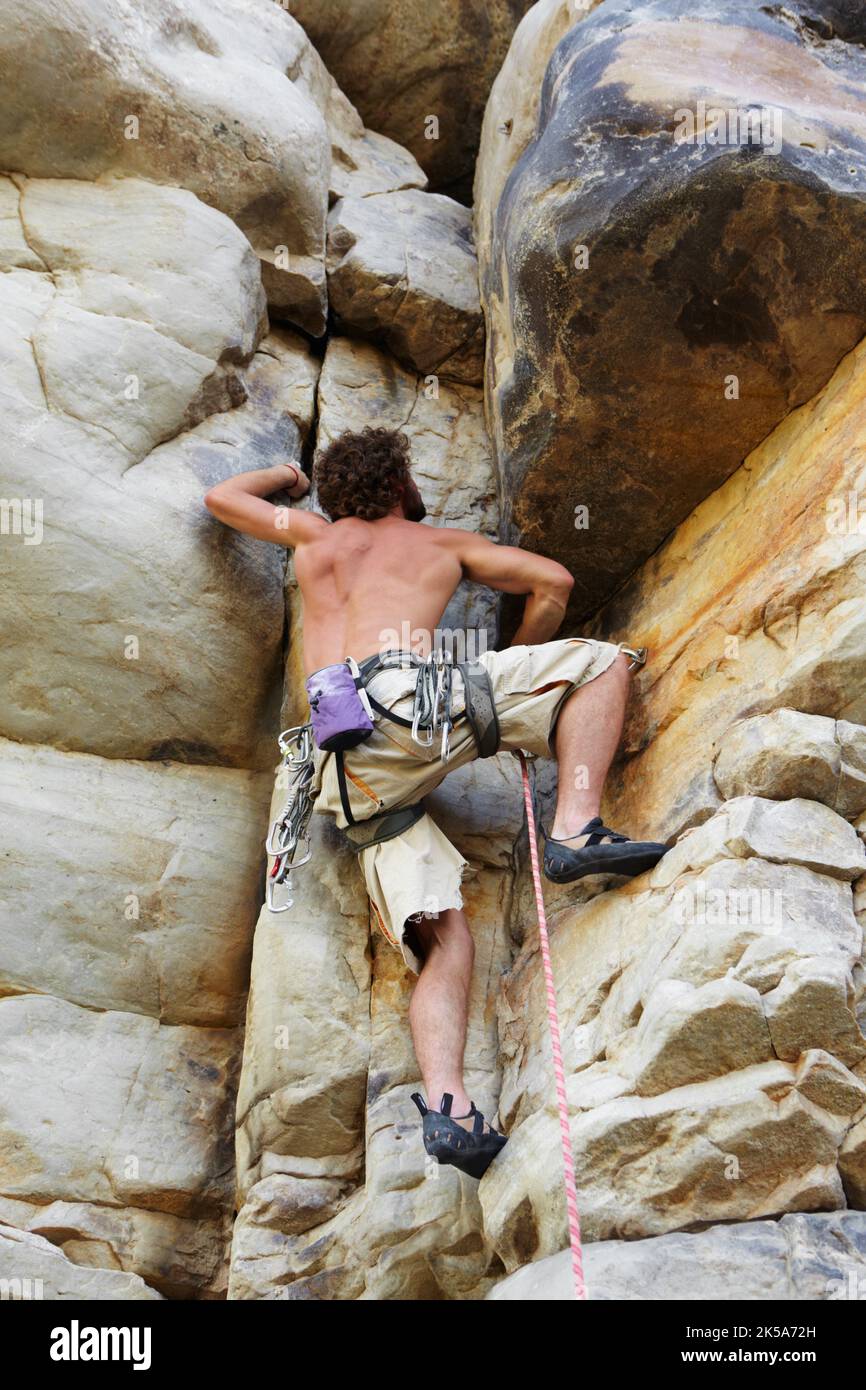 Cavando sus dedos en las grietas. Un escalador que sube por la cara de un acantilado. Foto de stock