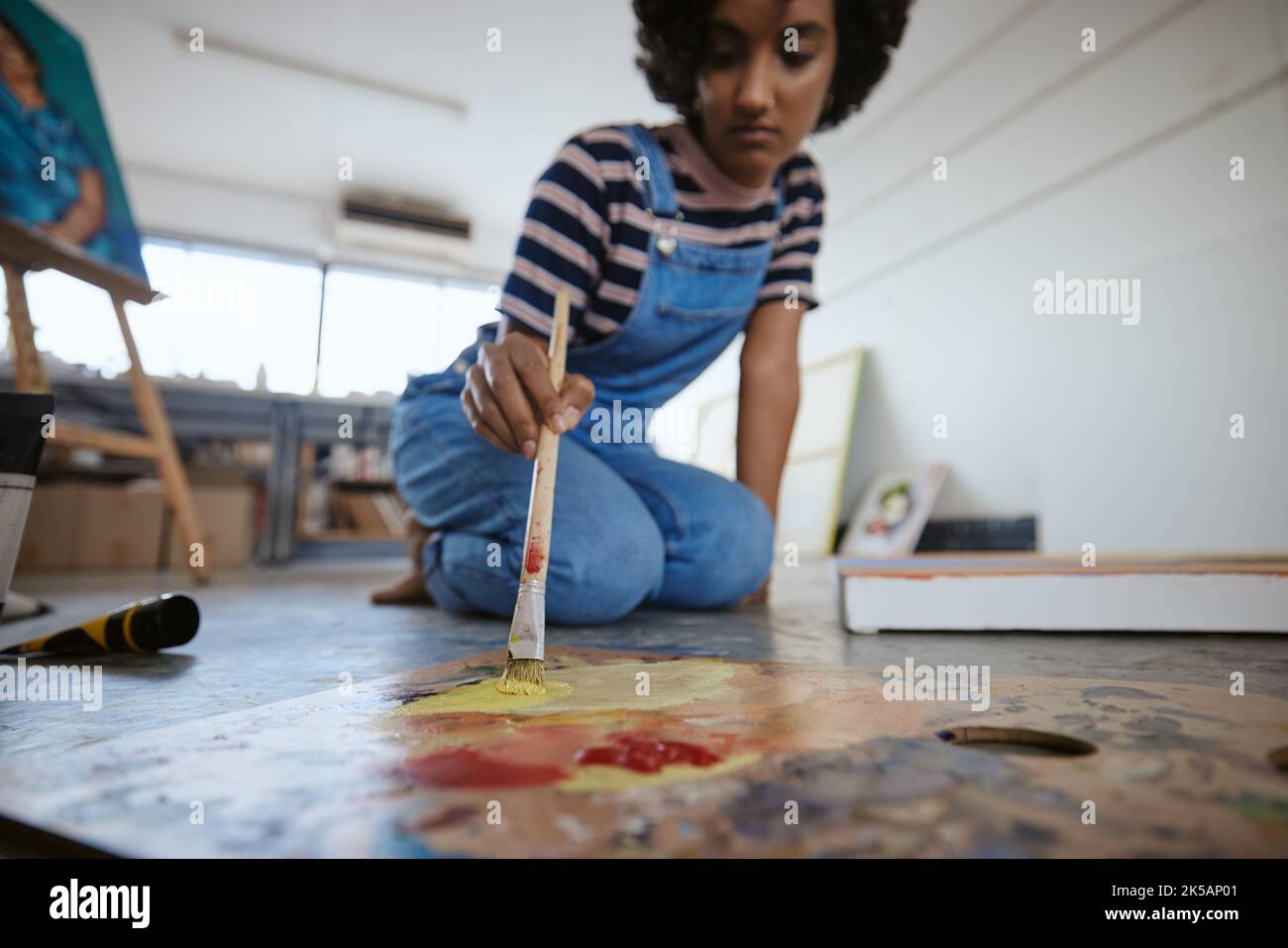 Mujer artista, pintura y lienzo en el piso en el estudio de arte para exposición creativa, la academia de diseño y los estudiantes taller de casa, escuela o galería Foto de stock