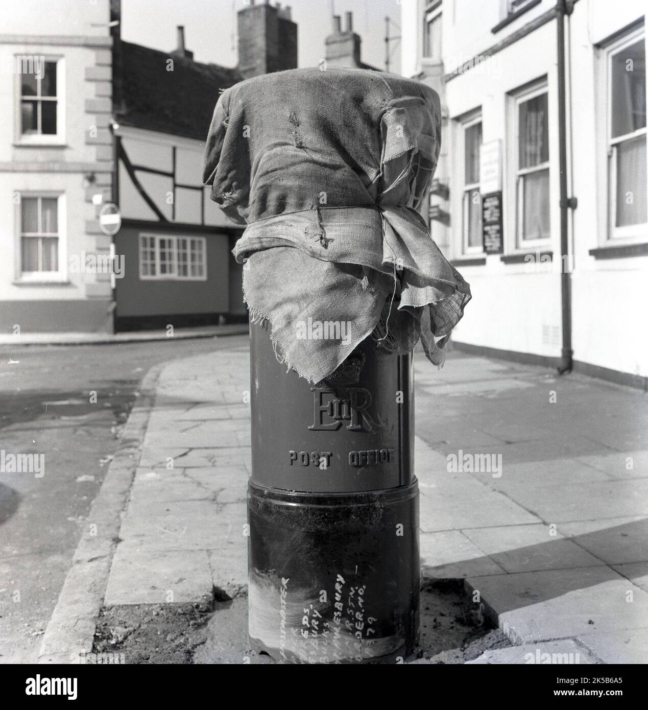 1964, histórico, sobre un pavimento, un pilar recién erigido o una caja de correos cubierto con viejos sacos postales, todavía no en uso, como su base de hormigón necesitaba para establecerse, Aylesbury, Inglaterra, Reino Unido. Foto de stock