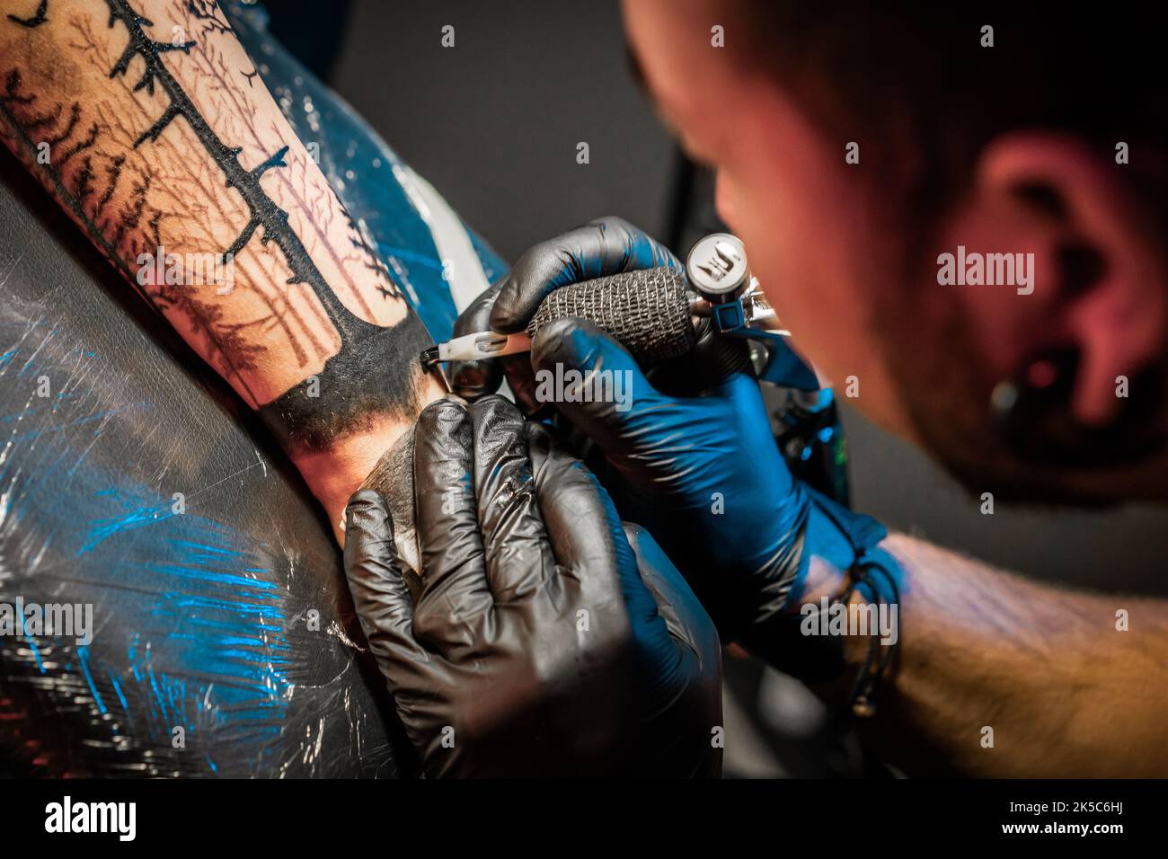 Retrato de hombre tatuaje maestro con dreadlocks mostrando el proceso de  creación tatuaje en el cuerpo femenino bajo la luz de la lámpara. Artista  profesional trabajando en el salón Fotografía de stock -