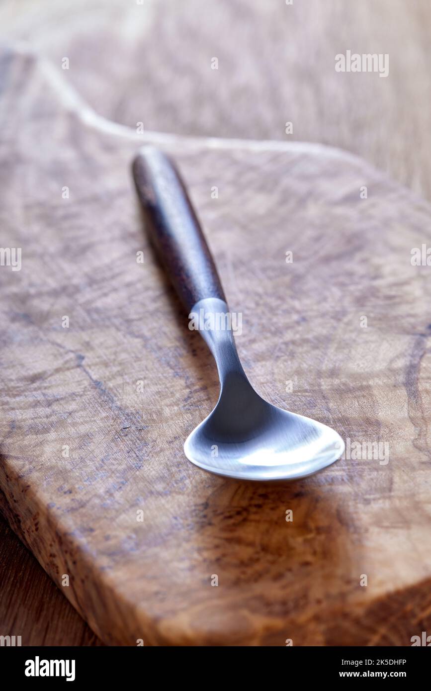 Una cucharilla vacía hecha de madera y metal sobre una tabla de cortar de madera de oliva - vista de cerca Foto de stock