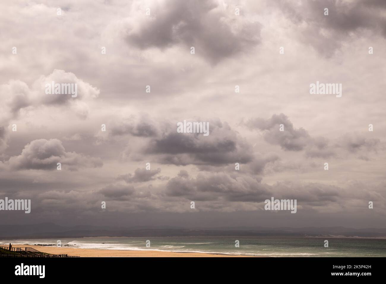 Moody y las nubes enojadas en una playa con la lluvia amenazando para bajar. Arena prístina y nubes gruesas Foto de stock
