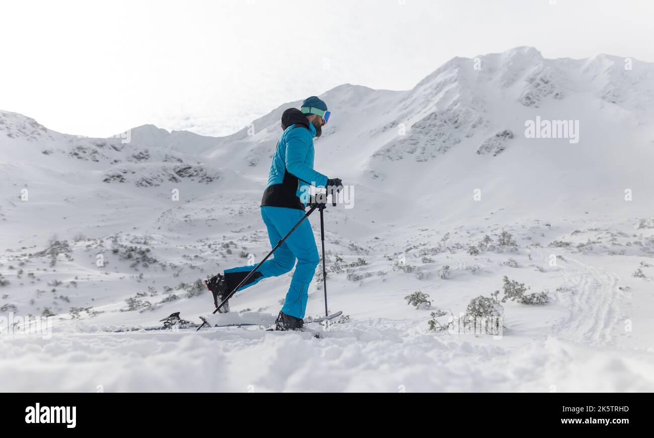 Hombre esquiador de campo a pie hasta la cumbre de un pico nevado en el Bajo Tatras en Eslovaquia. Foto de stock