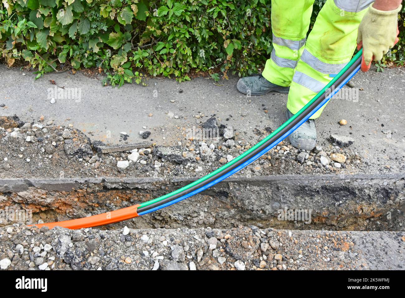 Cable de tecnología de Internet de banda ancha de alta velocidad de fibra óptica colocado bajo tierra en una estrecha zanja de pavimento poco profunda por el trabajador de infraestructura Essex UK Foto de stock