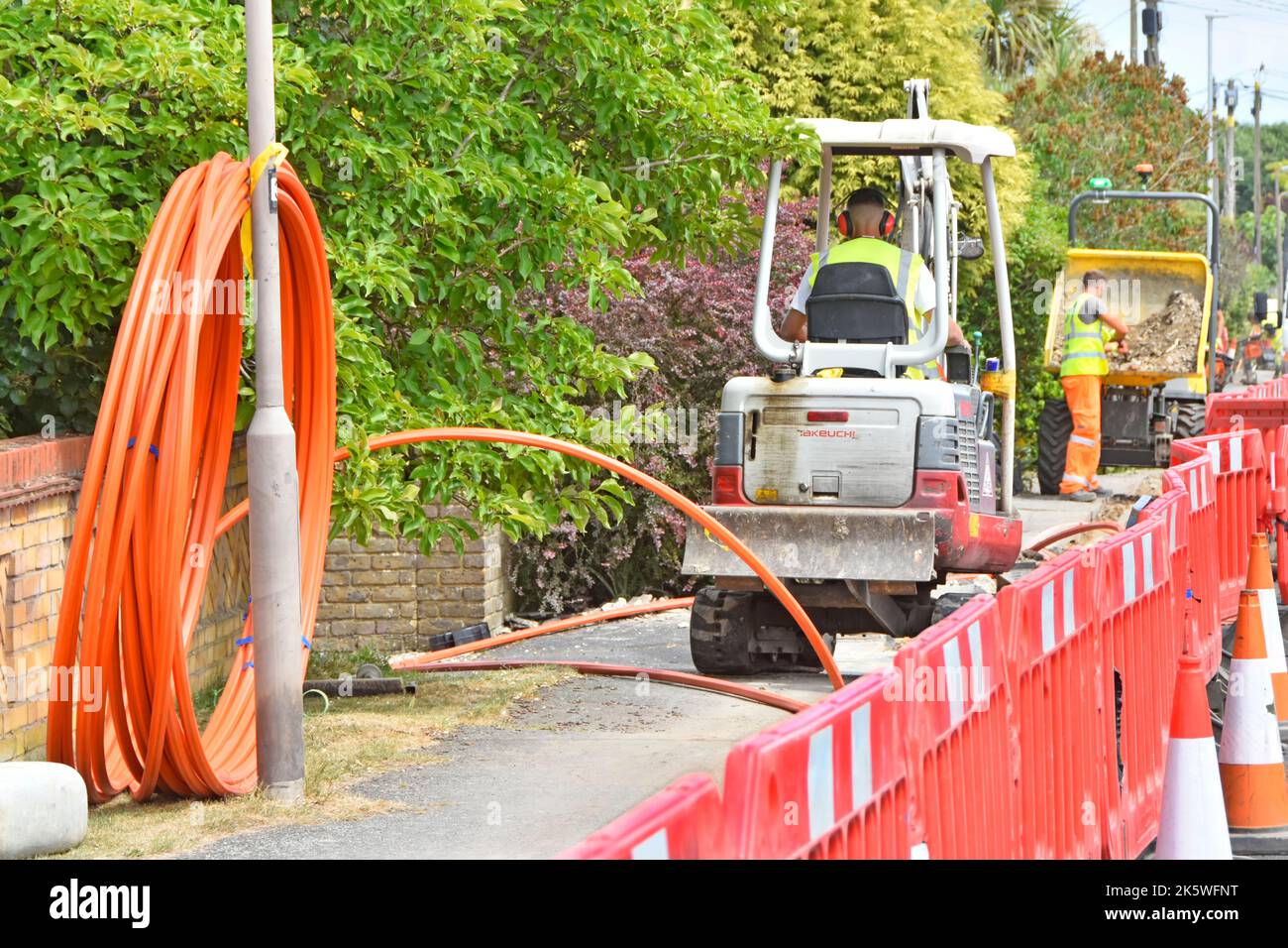 Interrupción a los propietarios de propiedades vehículos cerrados cruce caminos de entrada trabajadores máquinas tomar el pavimento de paso de los pies para el cable subterráneo de banda ancha Essex Reino Unido Foto de stock