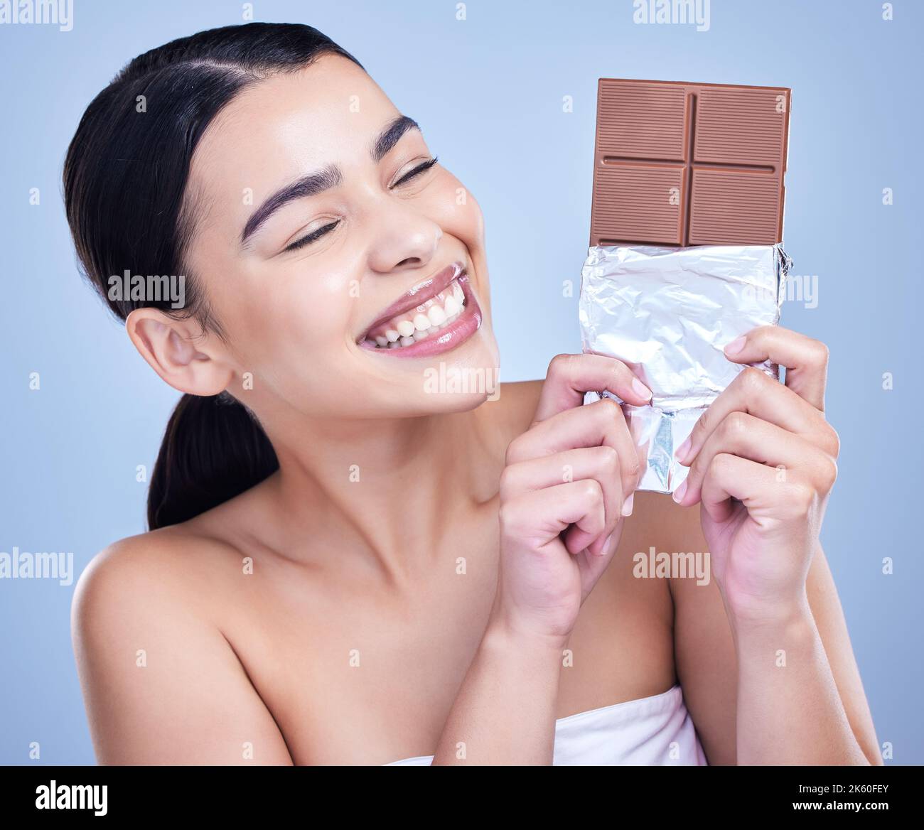 Una hermosa mujer de raza mixta sosteniendo una losa de chocolate. Bocado modelo hispano en el postre sobre un fondo azul de copyspace Foto de stock
