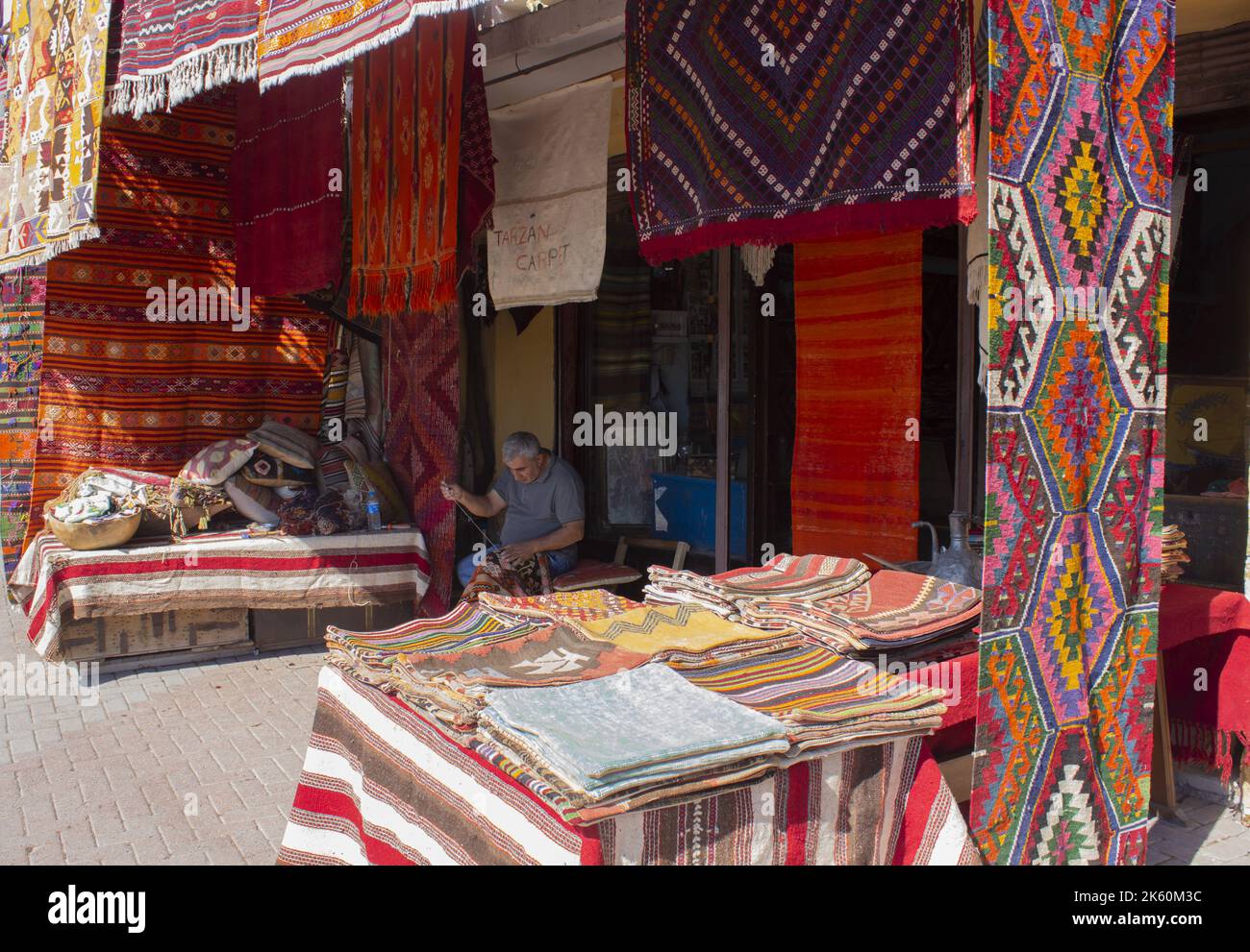 Bergama, Izmir, Turquía - 10.10.2022: Hombre tejiendo alfombras hechas a mano en frente de su tienda tradicional, el hombre de costura de alfombra tradicional Foto de stock
