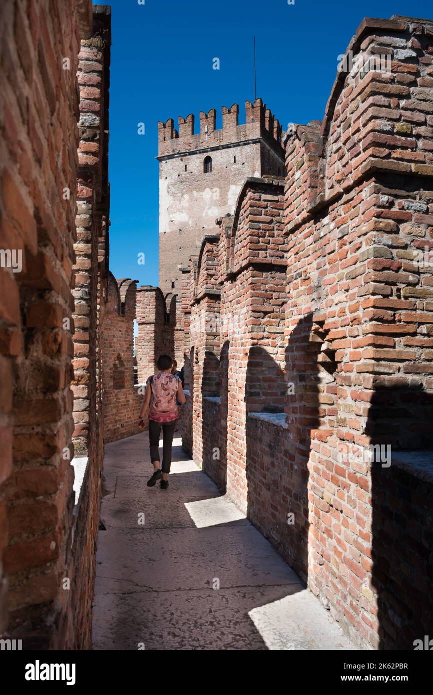 Muralla medieval del castillo de la ciudad, vista en verano de un turista en una pasarela para explorar las distintivas almenas de la cola de golondrinas de Castelvecchio, Verona Foto de stock