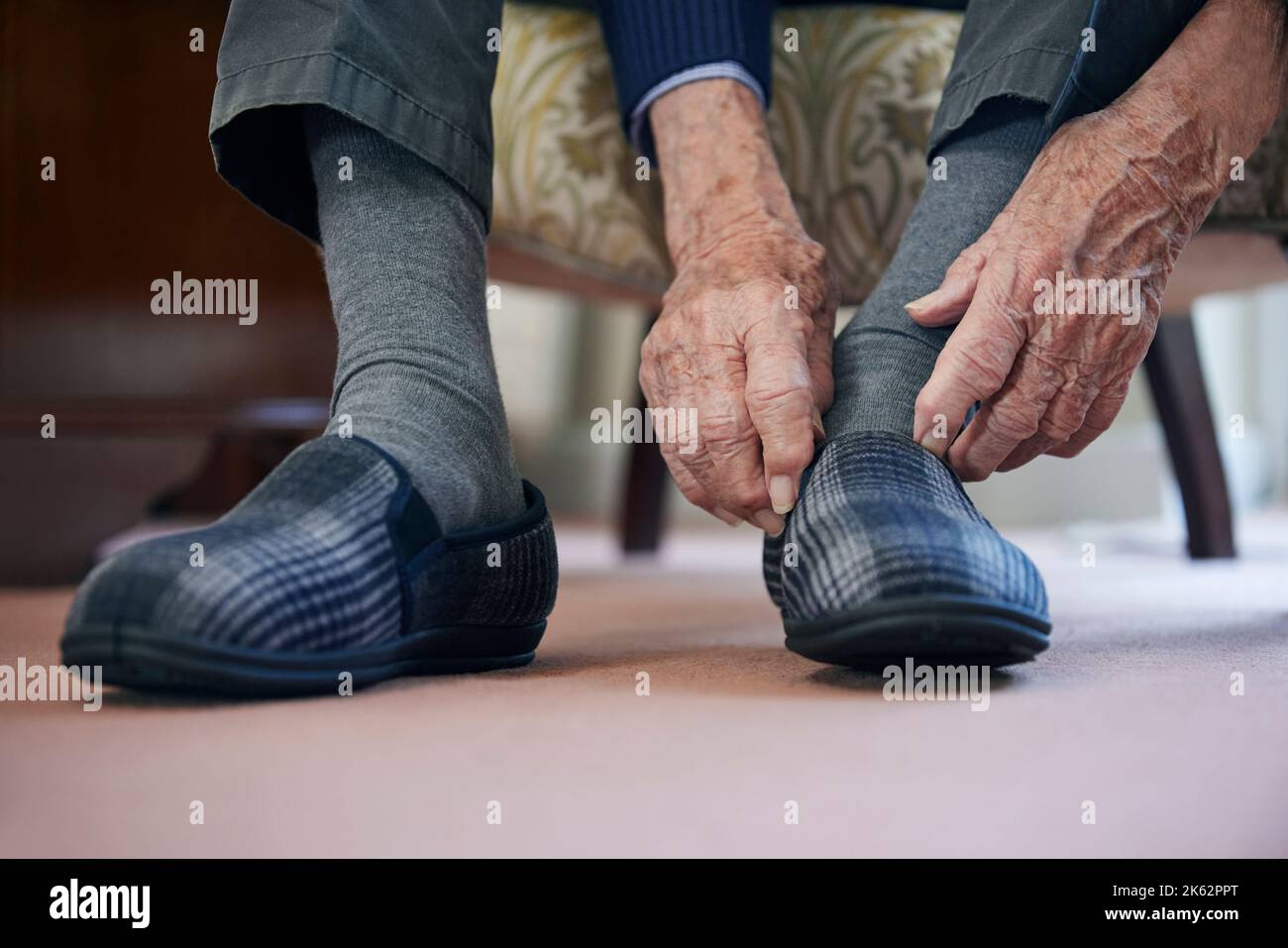 Primer plano del hombre mayor Poniendo zapatillas para mantener los pies calientes en el coste de la crisis de la vida Foto de stock