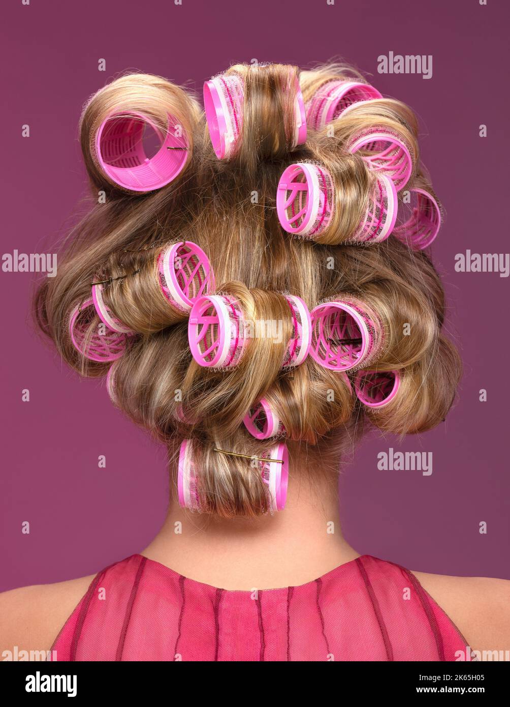 Rubia mujer hombros con rizadores rosas en su cabello Foto de stock