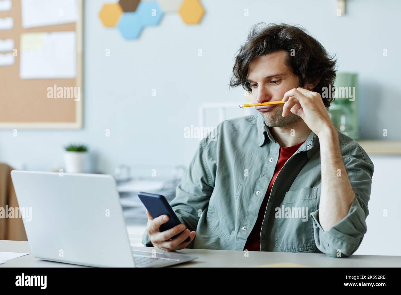 Retrato de un joven caucásico jugando con el lápiz y utilizando el teléfono en el lugar de trabajo que sufría aburrimiento y dilación Foto de stock