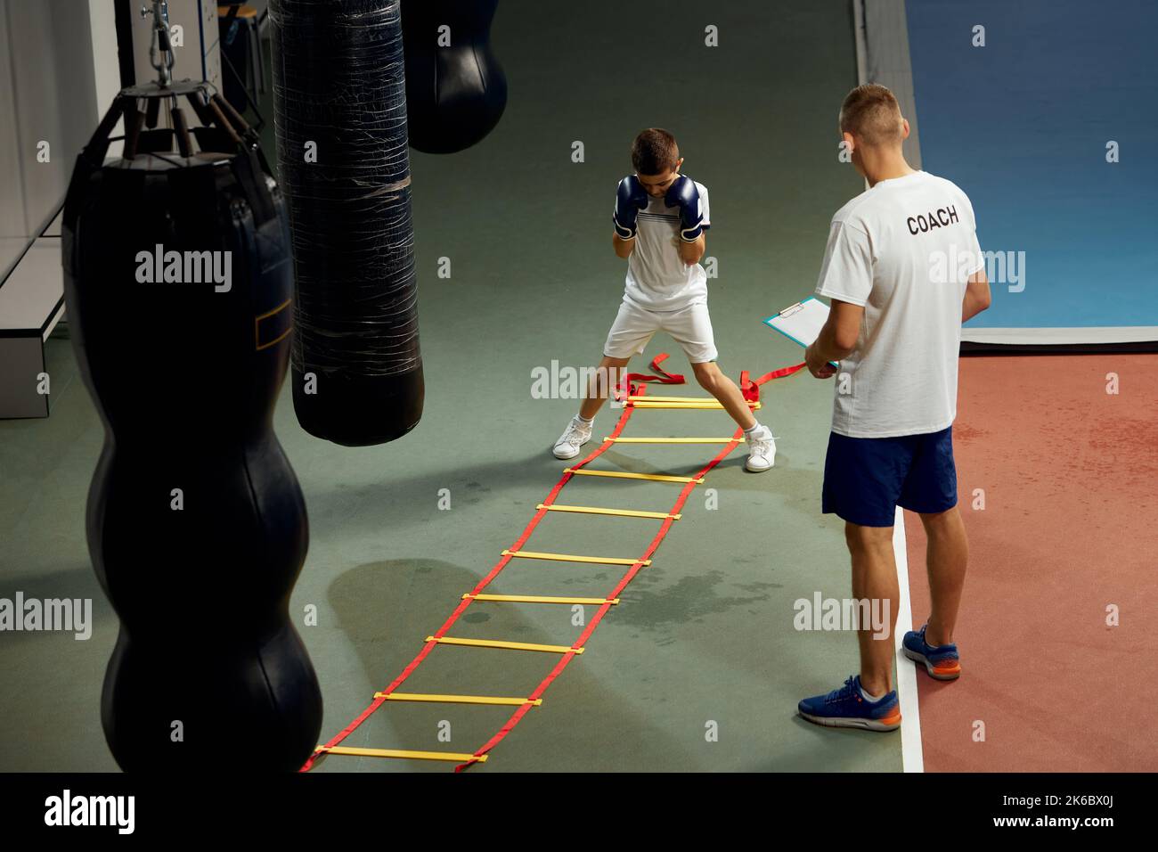 Dos atletas, el hijo y el padre están haciendo deportes en el gimnasio. Entrenamiento de boxer principiante con su entrenador ar boxing ring, en interiores. Deporte, potencia, energía y actividad Foto de stock