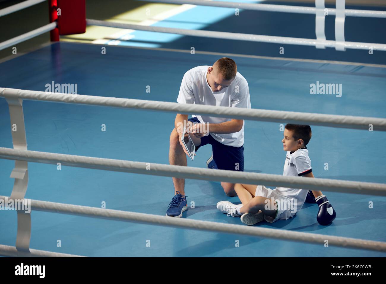 Dos atletas, el hijo y el padre están haciendo deportes en el gimnasio. Entrenamiento de boxer principiante con su entrenador ar boxing ring, en interiores. Deporte, potencia, energía y actividad Foto de stock