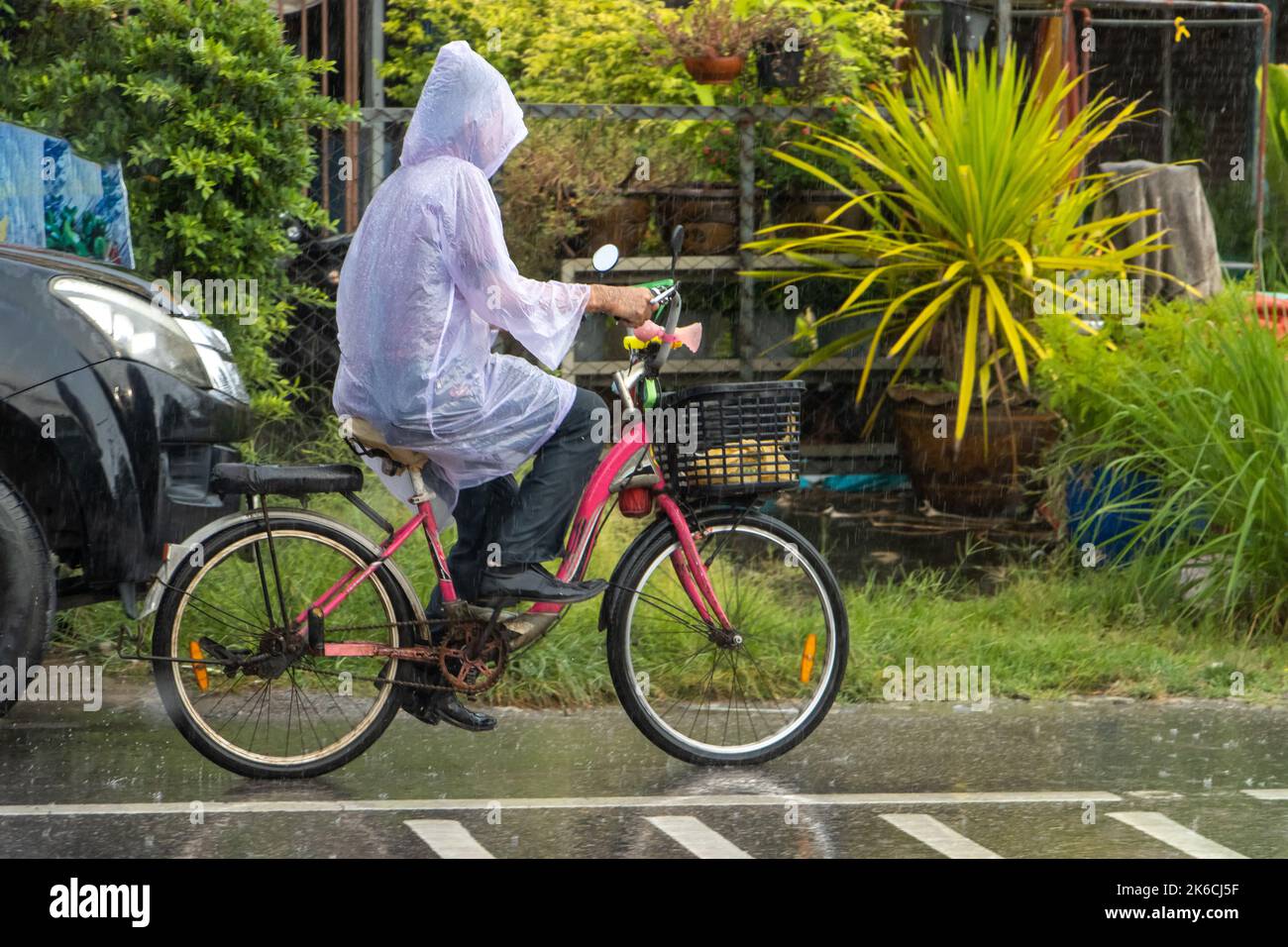 Un hombre con chubasquero monta en bicicleta por la calle bajo fuertes  lluvias, Tailandia Fotografía de stock - Alamy