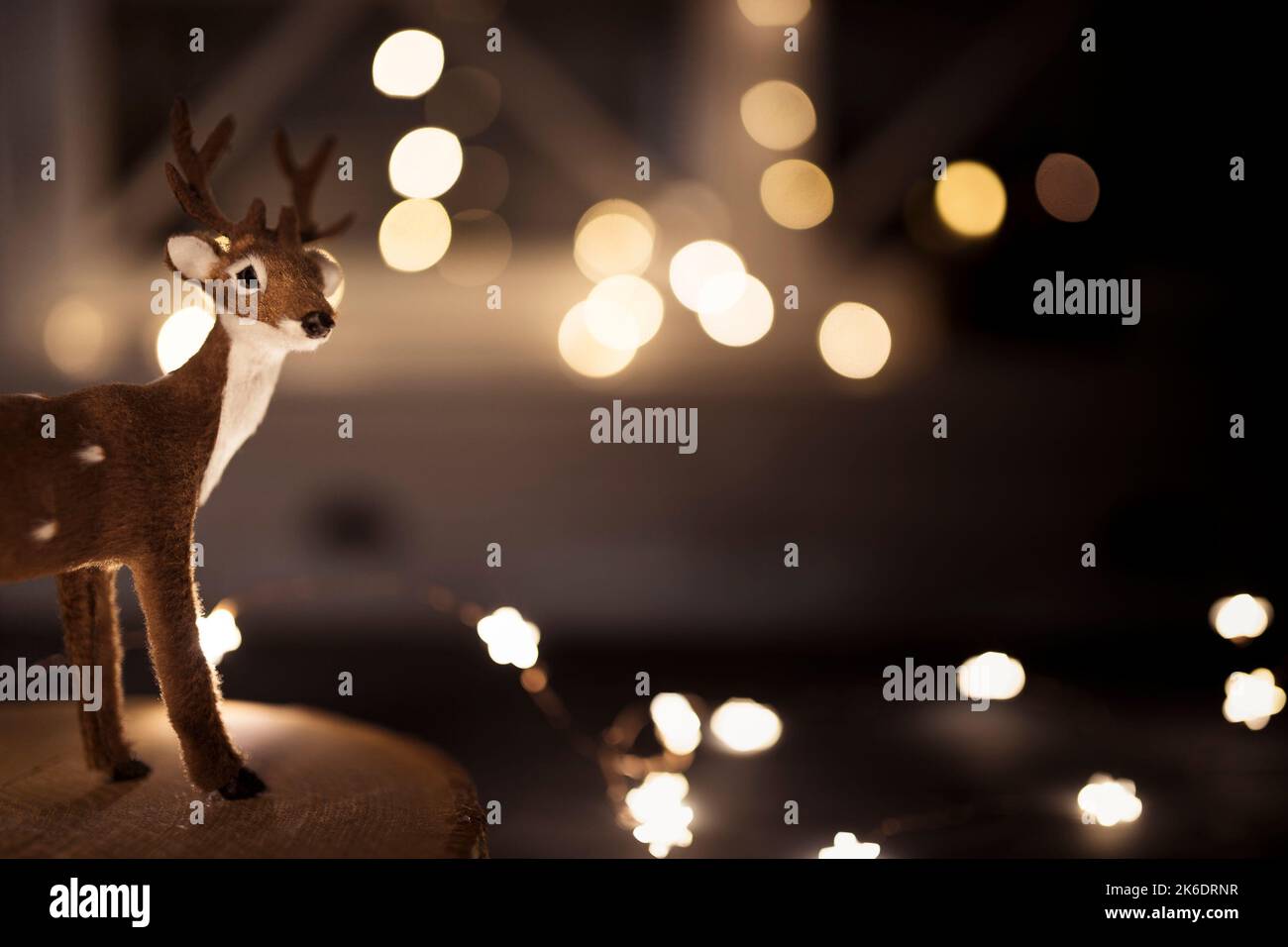 Reno en miniatura sobre bandeja de madera, con luces de cuerda brillantes en el fondo. Papel tapiz de Navidad con espacio para copias. Foto de stock