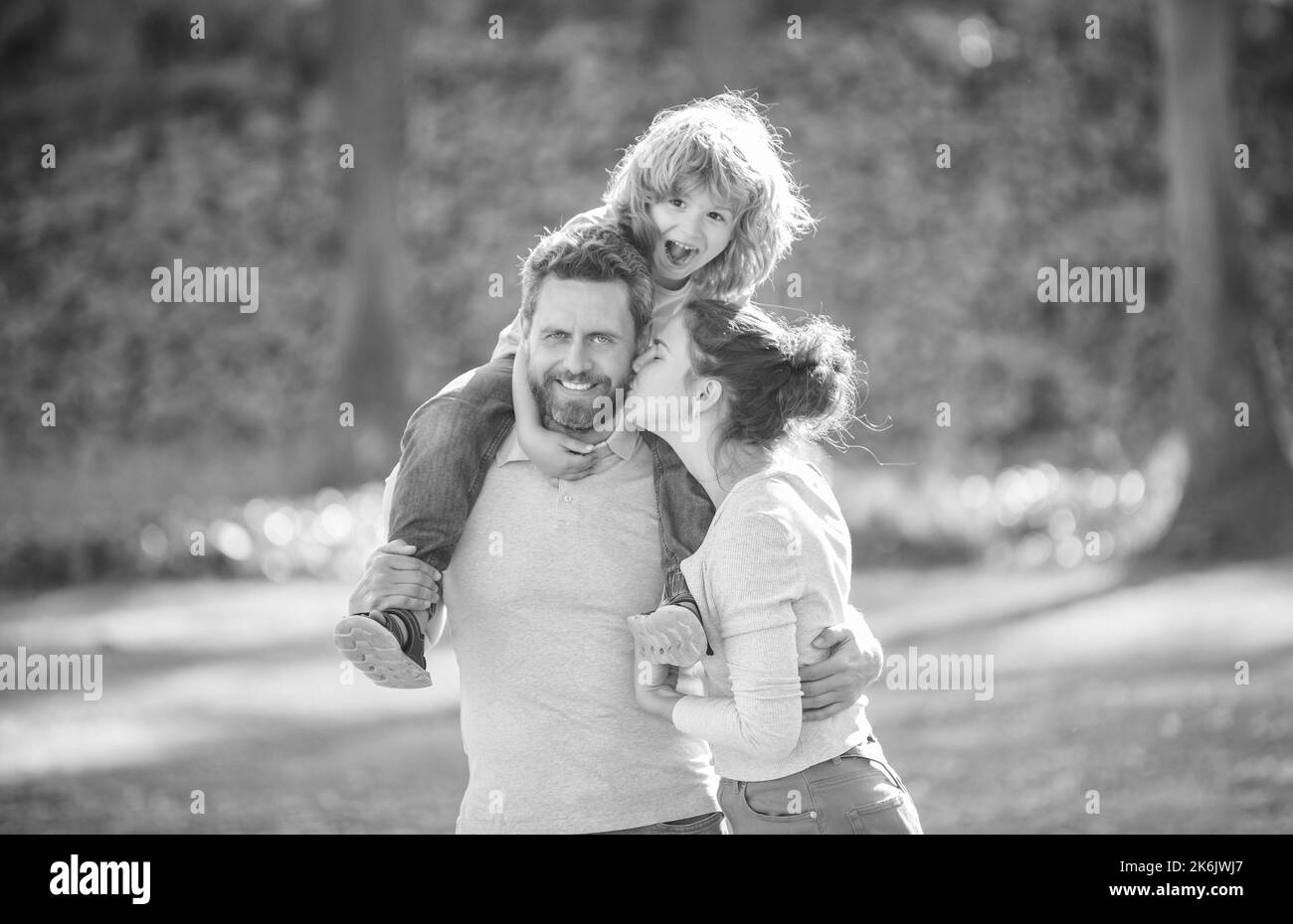 Madre beso padre mientras niño niño montar piggy detrás en los hombros de los padres verano al aire libre, familia Foto de stock