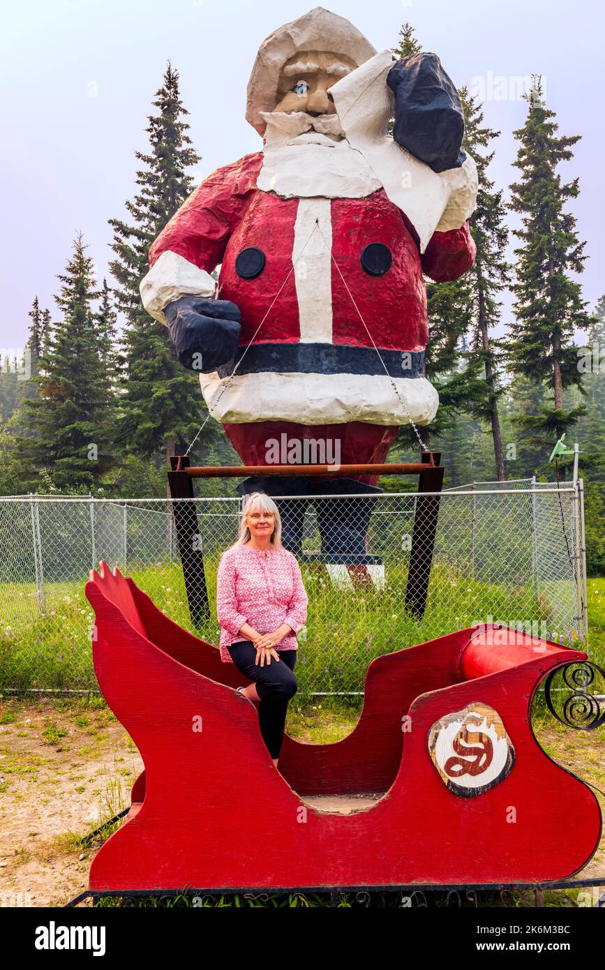 Mujer mayor posando con la estatua al aire libre enorme de Santa Claus; Polo Norte; Alaska; EE.UU. Foto de stock
