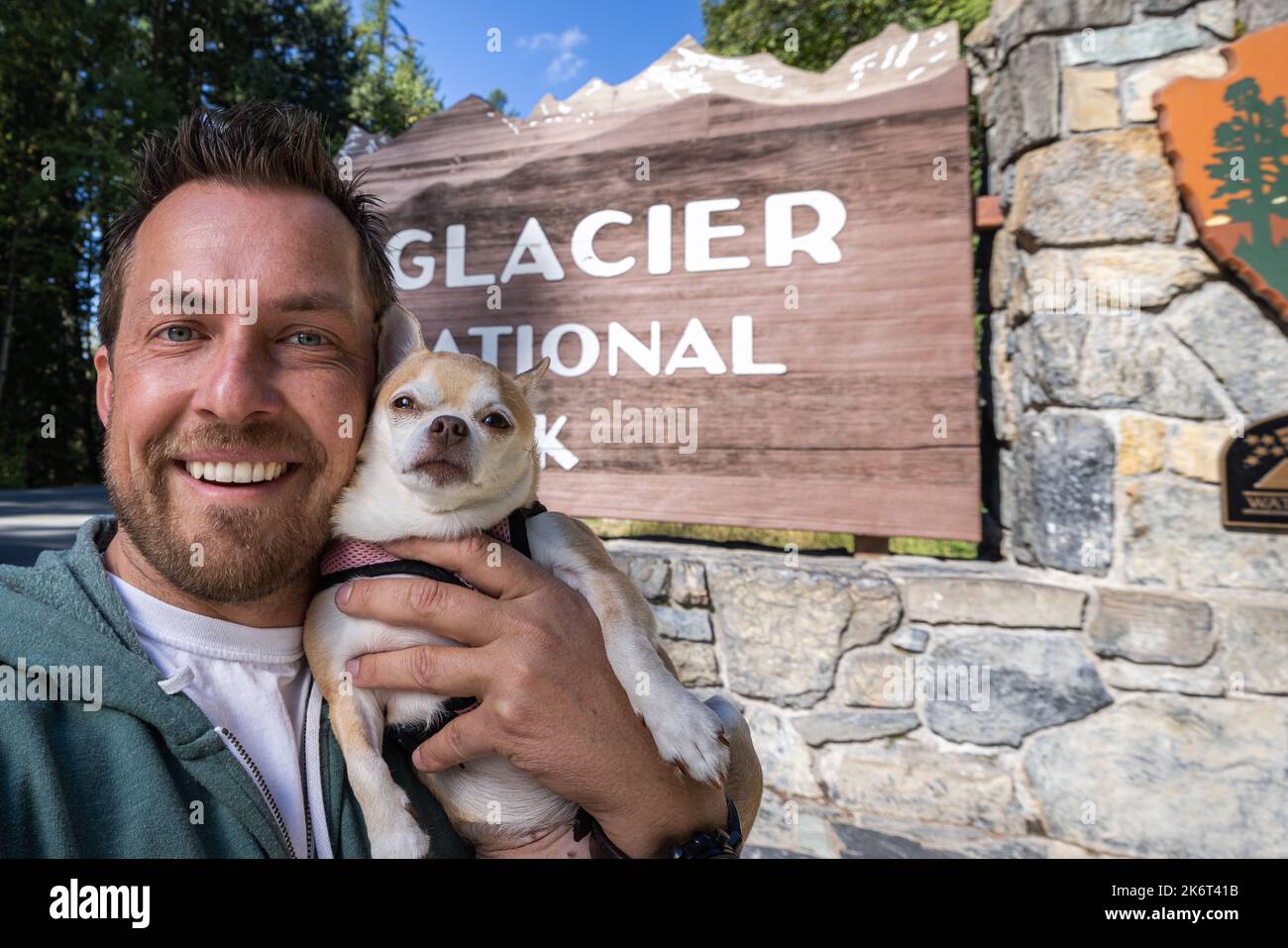 Hombre y su mejor amigo un chihuahua tomando un selfie delante de la señal de bienvenida para el Parque Nacional Glaciar en Montana Foto de stock