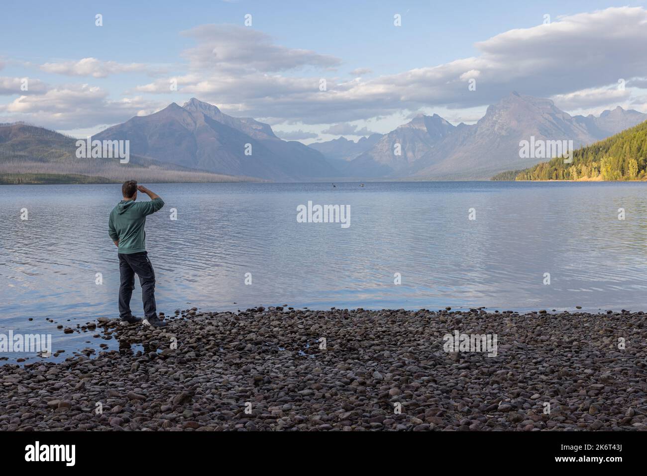 Hombre de pie en la costa mirando las increíbles montañas a través del lago McDonald en el Parque Nacional Glacier Foto de stock