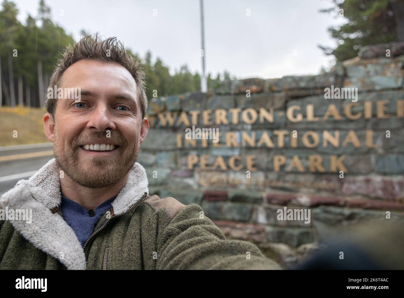 Hombre tomando un selfie frente a la entrada Waterton cerca de la frontera canadiense en el Parque Nacional Glacier Foto de stock