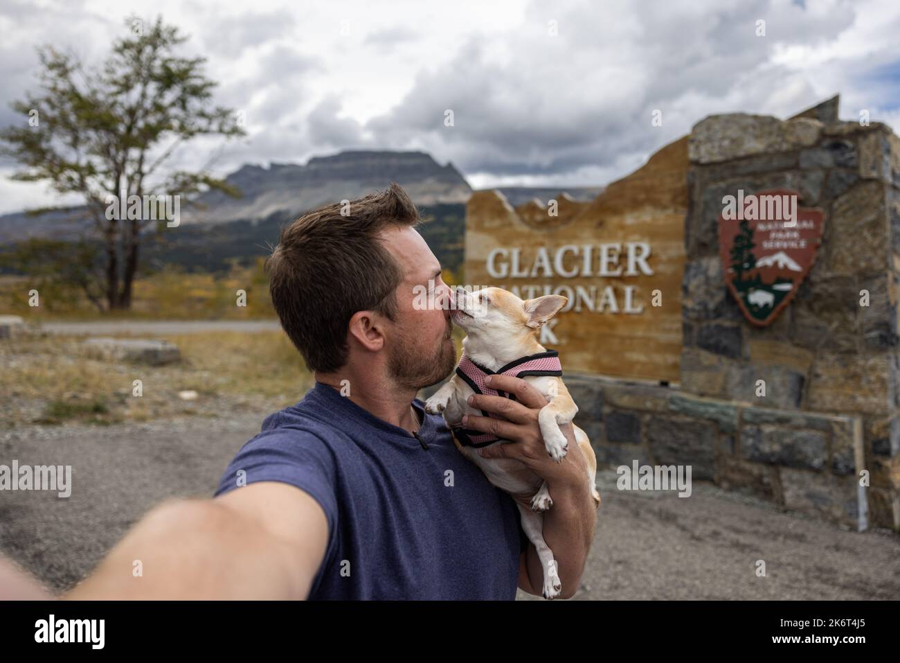 Hombre y su mejor amigo un chihuahua tomando un selfie delante de la señal de bienvenida para el Parque Nacional Glaciar en Montana Foto de stock