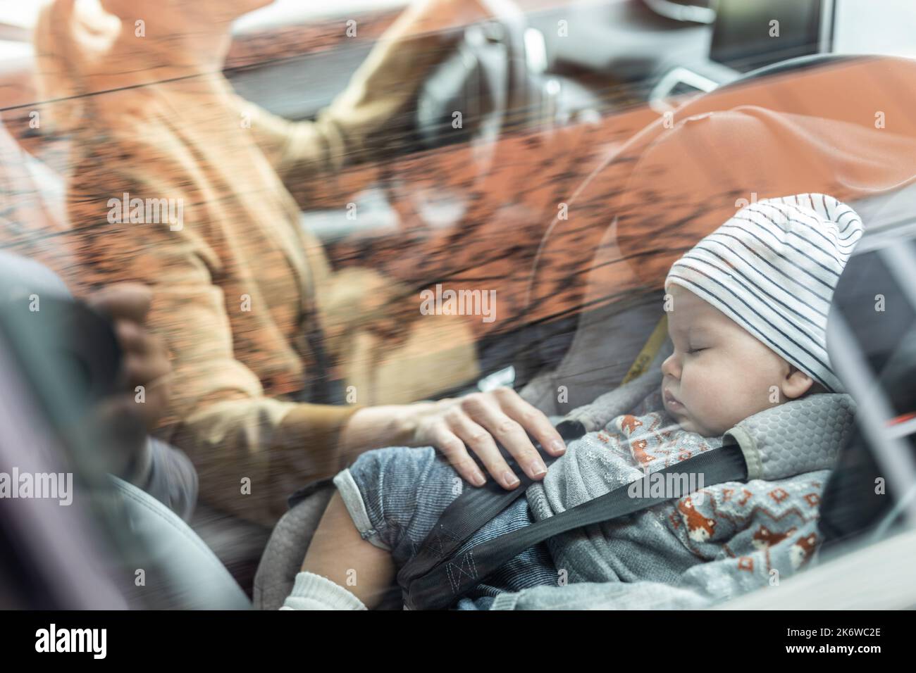 Madre que se concentra en conducir el coche de la familia mandando mientras que su bebé duerme en el asiento de coche del bebé cerca de su sitio. Foto de stock