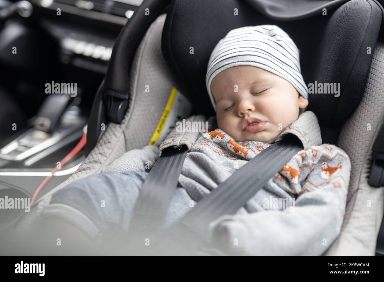 Lindo bebé niño durmiendo atado con correa en el asiento de seguridad para niños en el compartimiento de pasajeros durante la conducción del coche. Foto de stock