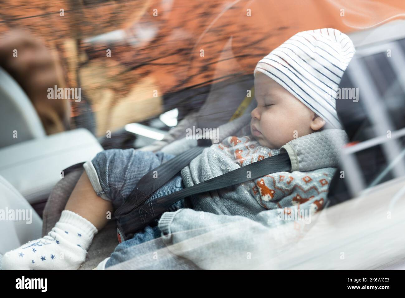 Lindo bebé niño durmiendo atado con correa en el asiento de seguridad para niños en el compartimiento de pasajeros durante la conducción del coche. Foto de stock