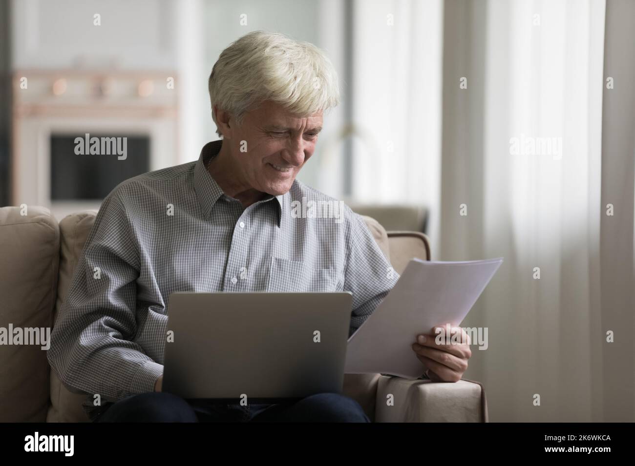 El hombre mayor utiliza el ordenador portátil, leer los documentos parece satisfecho Foto de stock