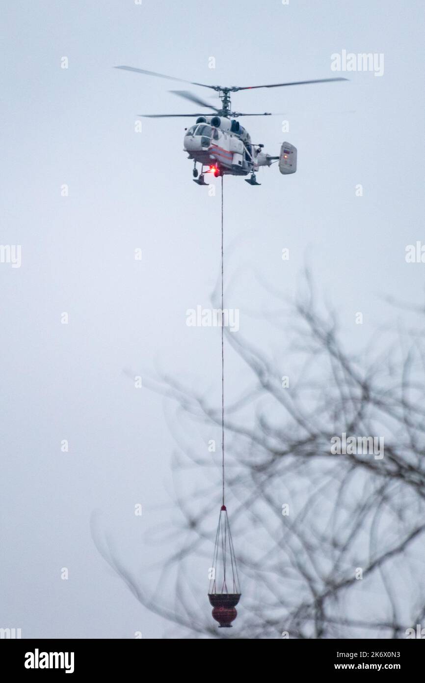 Un helicóptero contra incendios lleva un contenedor de agua para extinguir un incendio en un edificio de producción Foto de stock