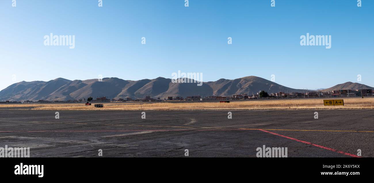 Pista de aterrizaje con vistas a las montañas, el suelo seco y amarillo en contraste con un hermoso cielo azul claro Foto de stock