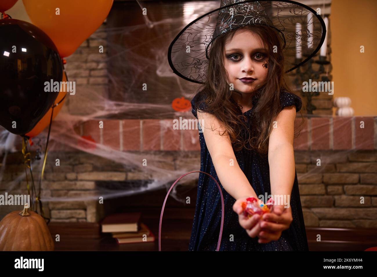 Hermosa niña con maquillaje de ojos ahumados, en sombrero de mago, posa contra una pared cubierta de telaraña con golosinas de Halloween Fotografía de stock - Alamy Hermosa niña con maquillaje de ojos ahumados, en sombrero de mago, posa contra una pared cubierta de telaraña con golosinas de Halloween Fotografía de stock - Alamy