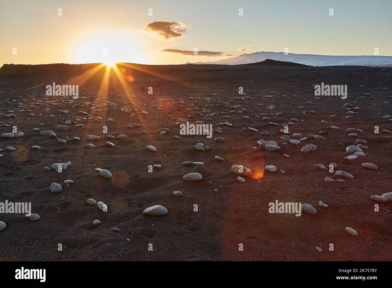 Islandia paisaje playa de arena negra con piedras y llamarada puesta de sol Foto de stock