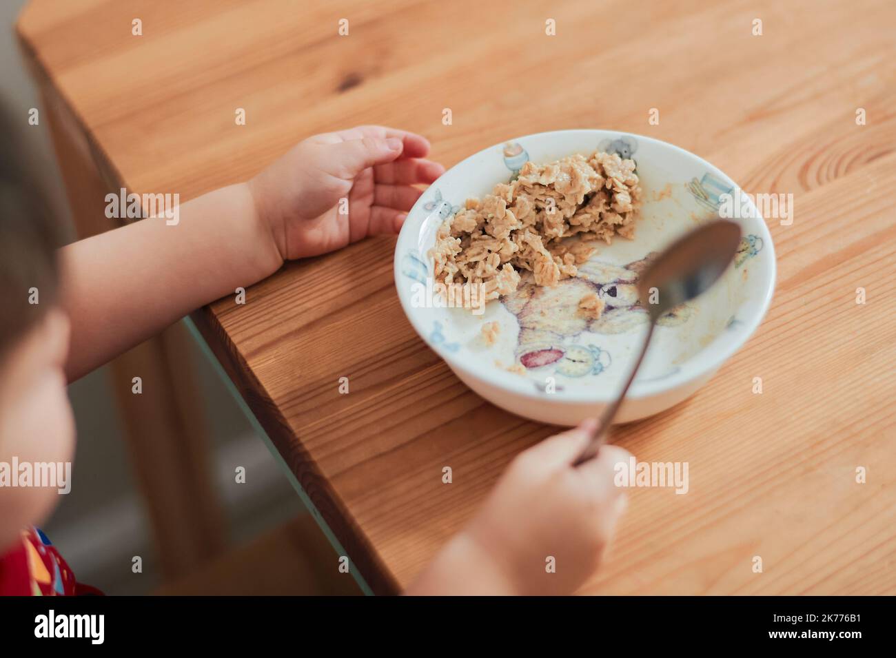 Un niño está comiendo avena para el desayuno en la mesa de la cocina Foto de stock