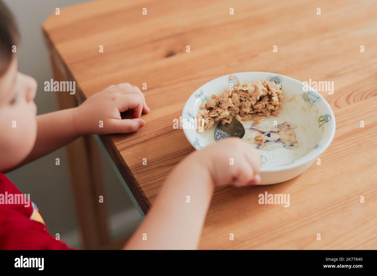 Un niño está comiendo avena para el desayuno en la mesa de la cocina Foto de stock