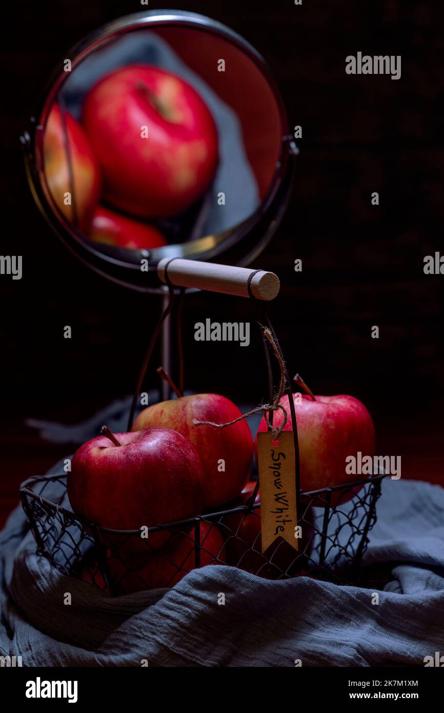 Una cesta de manzanas rojas con la inscripción Blancanieves se refleja en un espejo, recreando la atmósfera del cuento de hadas de Blancanieves Foto de stock