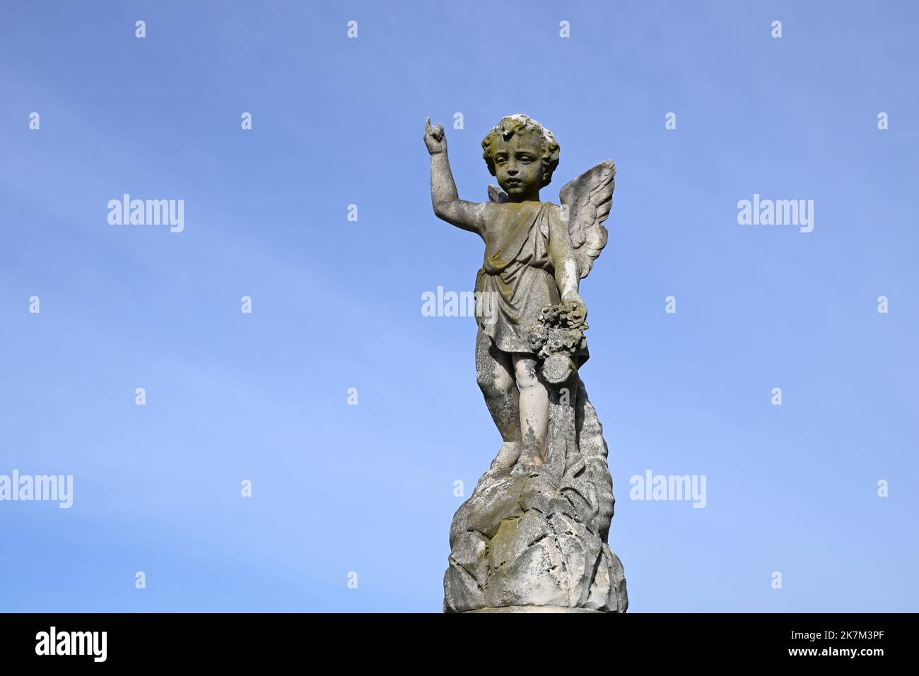 El querubín, o ángel niño, escultura hecha de piedra, apuntando hacia los cielos con el cielo azul en el fondo Foto de stock