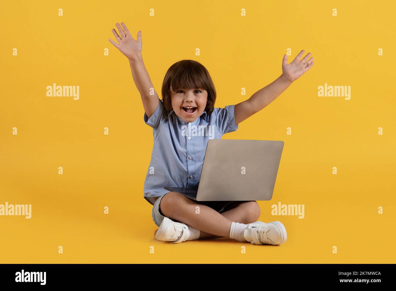 Gran educación del Internet. Niño excitado estudiando en línea en el ordenador portátil y gritando hooray, disfrutando el aprendizaje a distancia Foto de stock