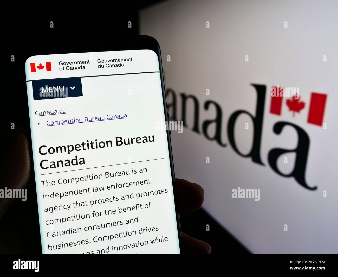 Persona con smartphone con sitio web del regulador canadiense Competition Bureau en pantalla delante del logotipo. Enfoque en el centro de la pantalla del teléfono. Foto de stock